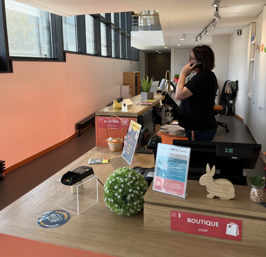 Accueil du musée avec une médiatrice au téléphone derrière le comptoir.
