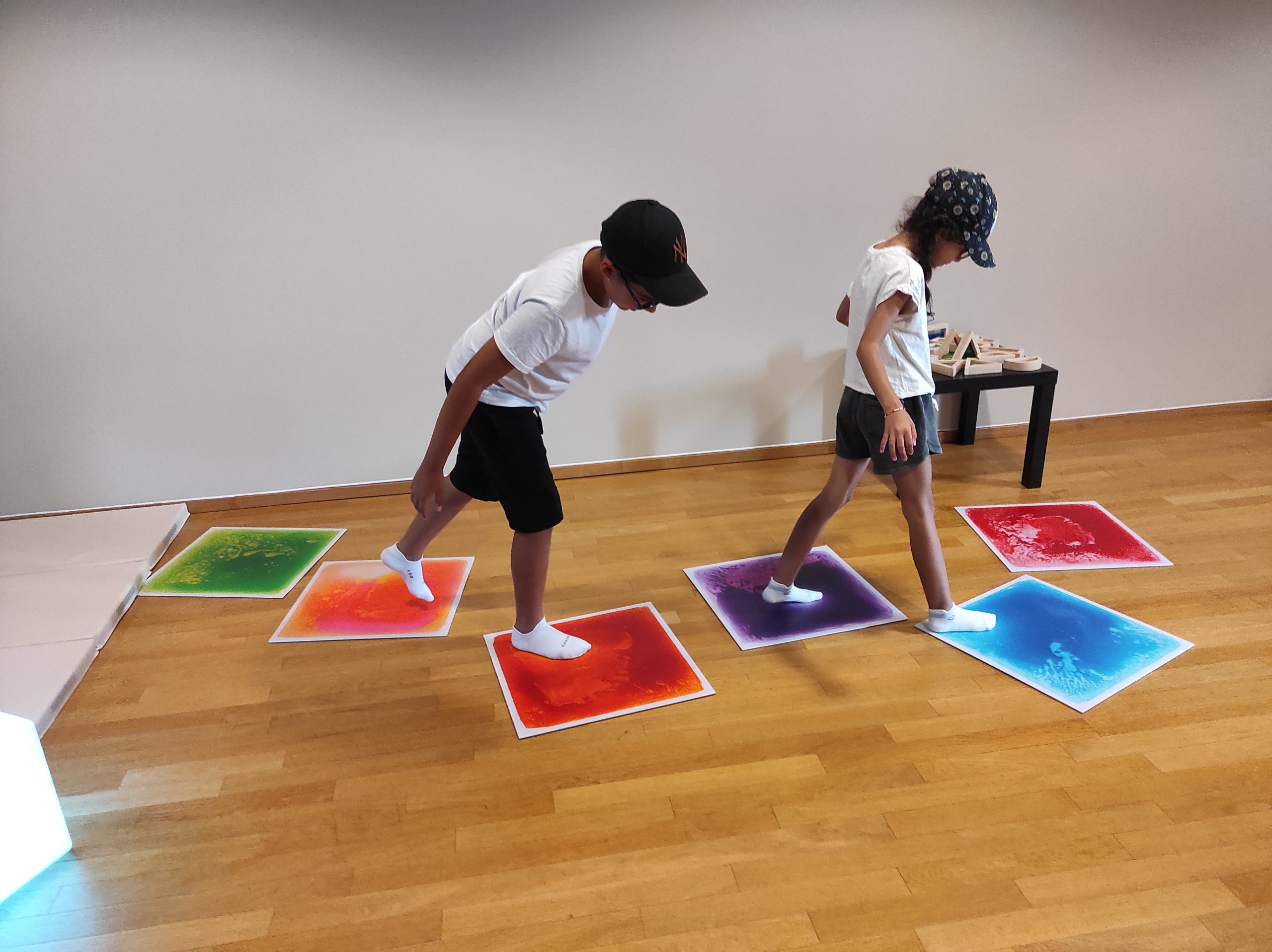 Deux enfants jouant à la marelle sur des carrés multicolores dans la salle dédiée aux enfants du musée.