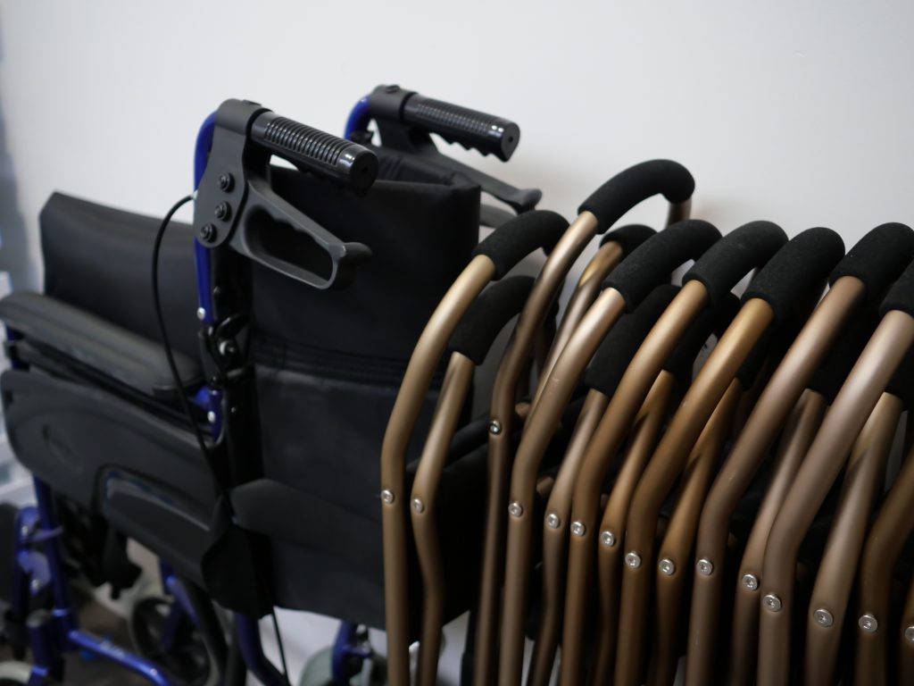 Un fauteuil roulant plié à côté d’une chaise pliable, rangés dans le musée.